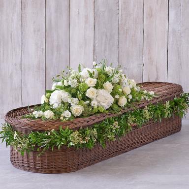 Detailed photo of a large standing floral cross made entirely of dense white carnations and greenery, placed on an easel in a chapel.