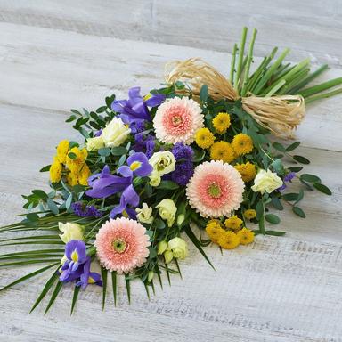 A traditional standing spray arrangement of white gladiolus and deep burgundy carnations placed respectfully near a wooden casket during a formal funeral service, soft overhead lighting.
